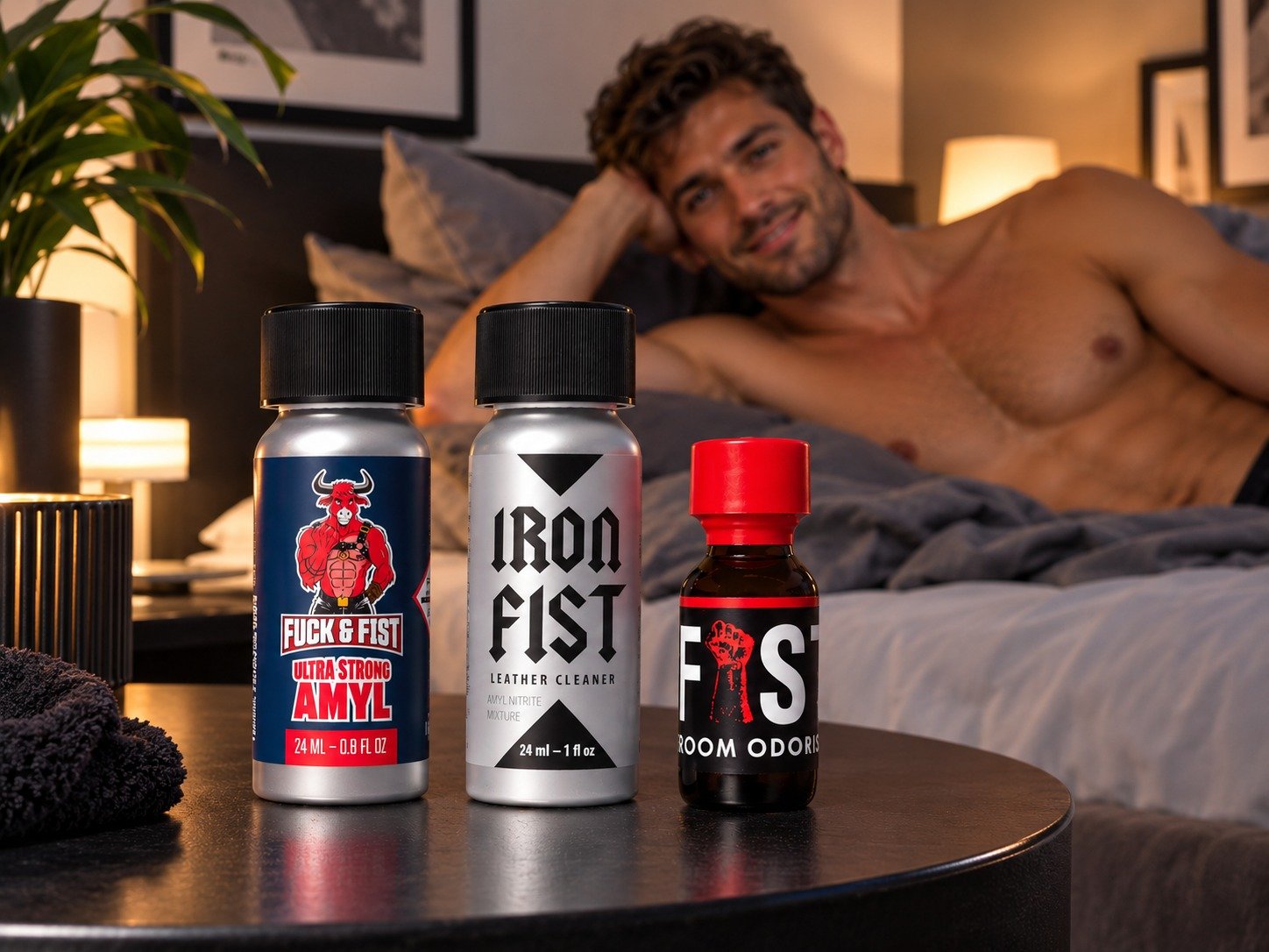 Homme nu sur le lit, regardant vers l’appareil photo, derrière trois flacons lubrifiants et nettoyants, en premier plan.